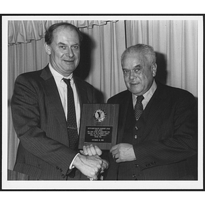 Two men posing while holding plaque and shaking hands