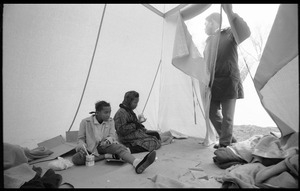Inside of a strikers' tent, two young women seated on the ground, a man standing in the entryway