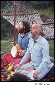 Ram Dass teaching in a half lotus with Krishna Das on his right