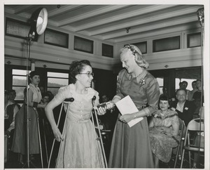 Margaret Milbank Bogert presents a small book to a girl using crutches