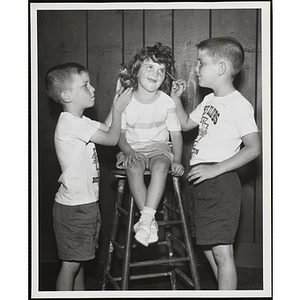 A boy rolls his sister's hair while another puts makeup on her during a Boys' Club Little Sister Contest