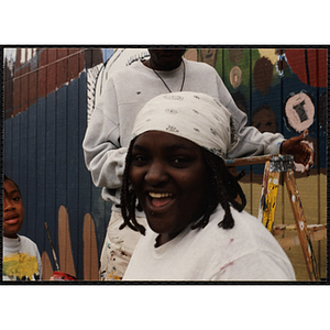 An African American woman from the Roxbury Boys & Girls Club smiling for the camera while painting a mural with other members
