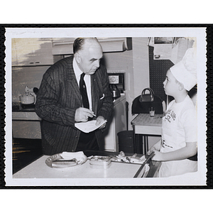 An unidentified man addresses a member of the Tom Pappas Chefs' Club in a kitchen