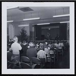 An audience of boys watch a clown on stage at a Christmas party