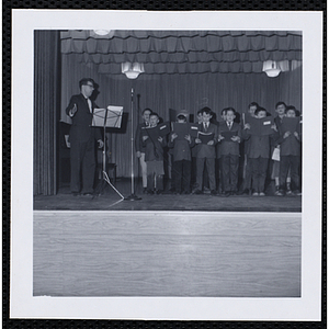 A man directs a boys' choir on a stage at a Christmas party