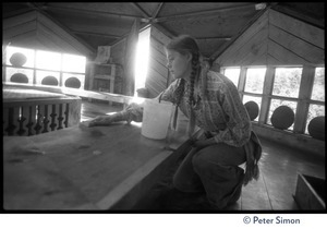Young woman kneeling in a communal dining hall, cleaning tables, Lama Foundation