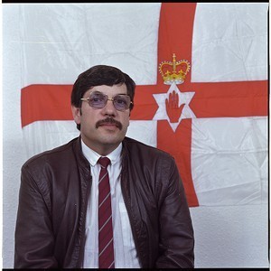 Andy Tyrie, UDA Supreme Commander, in front of Ulster flag in UDA Headquarters, Gawn St., Newtownards Road, Belfast