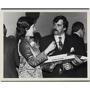 A woman holds a book titled "In Praise of Sailors" while talking to a man at a Boys' Clubs of Boston event