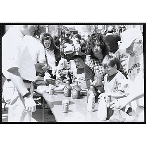 Two men and several children standing at tables with hot dogs and ketchup and mustard bottles at the Boys and Girls Clubs of Boston 100th Anniversary Celebration Street Fair