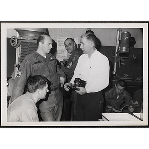 A photography instructor holds a camera and talks with one of the men in U.S. Army uniform at a photographic laboratory