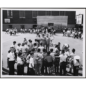 Children square dance on a playground as another group of children looks on during day camp