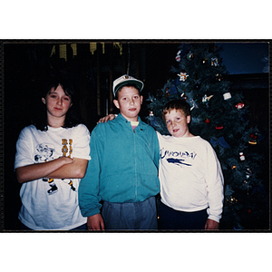 A girl and two boys pose in front of a Christmas tree