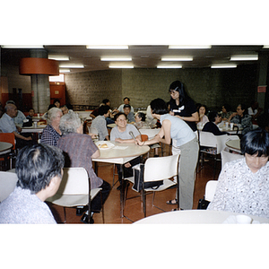 Woman offers a microphone to a table of women during a Chinese Resident Association meeting