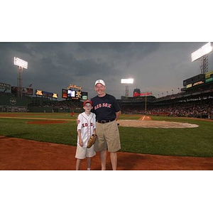 A man and a boy pose together on the field at Fenway Park