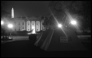 Nighttime view of the tents, one with a sign reading 'Houses not tents,' the White House and Washington Monument in the background