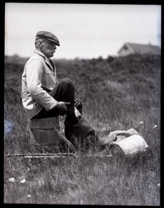 Otis Fish, the blind clam digger of Falmouth: portrait of Fish seated on a overturned bucket, putting on his wading boots