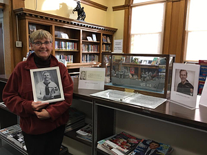 Daughter of Roy Olofson. Mr. Olofson built the ship pictured. It's a replica of the LST 310 that he served on in WWII. It's been donated to the library's museum by the family. She is holding a picture of her father.