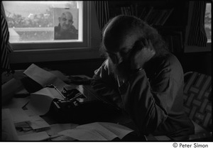 Ram Dass at typewriter: Ram Dass resting his face on his hand, with a portrait of Neem Karoli Baba in the background