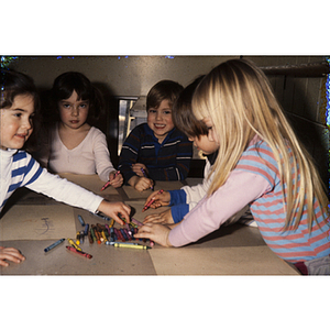 Young children sitting at a table choosing crayons