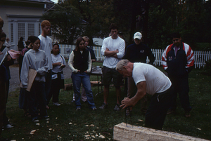 Hopkins Forest Fall Festival, 2000. Richard Babcock shapes a beam. Some identifications left to right: Nick Nelson (Class of 2003) red hair and white tee-shirt; Angus Beal (Class of 2003) in blue shorts and white long-sleeved tee-shirt, Kimberley Kemper (Class of 2003) in white baseball cap.