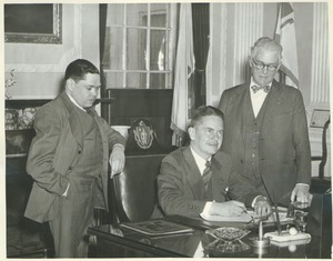 Governor Bradford signing the bill to change the name to University of Massachusetts, Senator Ralph C. Mahar, and President Hugh Potter Baker looking on