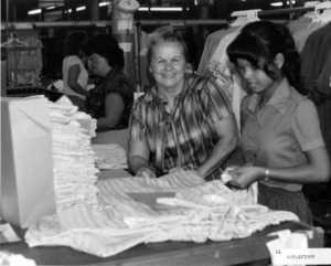 Photograph of women looking at fabric, [1982-1983].