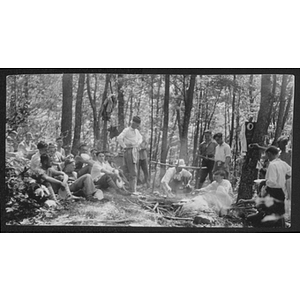 Young men sitting and standing around fire in the woods