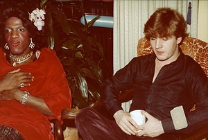 A Photograph of Marsha P. Johnson Sitting with Another Person, Wearing a Red Dress and Floral Hair Clip