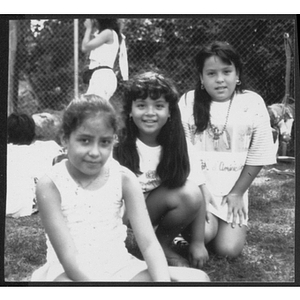 Three girls pose while seated outside in larger group