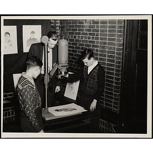 A boy using an enlarger while a man and another boy look on at a photographic laboratory