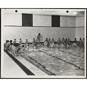 A man oversees boys competing in a tug-of-war in a natatorium pool as other boys look on poolside