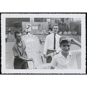 Two young men carrying a decorative chair whose back reads "MISS SOUTH BOSTON" during a Boys' Club Little Sister Contest