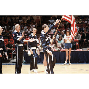 USA Men's Volleyball Team member steps forward and raises his hand, while his teammates stand in a line behind him and applaud