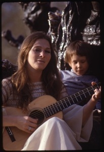 Judy Collins seated at the base of a statue, playing guitar for children