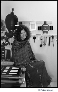 Usha (Cathy Brown) seated on a counter next to an enlarger in a darkroom