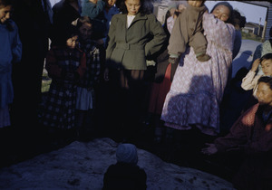 Eskimo women and children around a child on a blanket