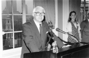 Suffolk University Dean John F. Brennan (SOM 1991-2001), standing behind podium with microphones
