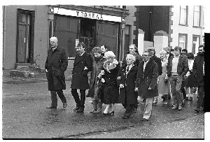 Funeral of Kevin Cunningham, shopkeeper and traditional musician, Dundrum, Co. Down. Includes shots inside the Church showing many musicians among the mourners