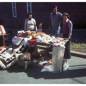 Three women and a man smiling, standing behind a table selling decorative arts and crafts at a Latino street festival
