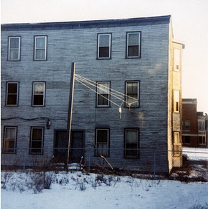 Exterior view of the back of three-story wooden residential building with paint peeling, in Roxbury, Mass.