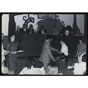 A man presents a trophy to a boy and shakes his hand while others look on during a Boys' Clubs of Boston Awards Night