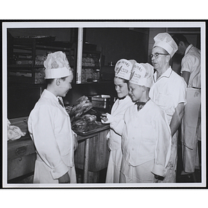 Three members of the Tom Pappas Chefs' Club handle roasted chickens as a Brandeis University kitchen staff member looks on