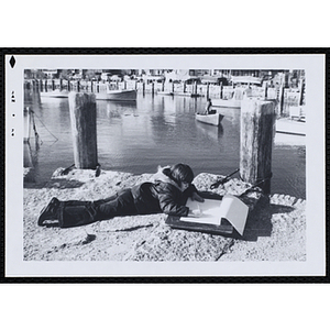 A boy makes a pencil drawing on a pier in Rockport