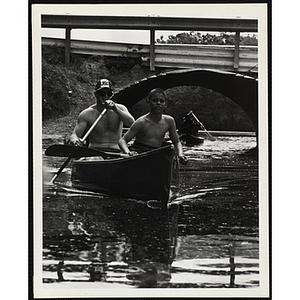 A Young adult and a boy paddle a canoe on a river