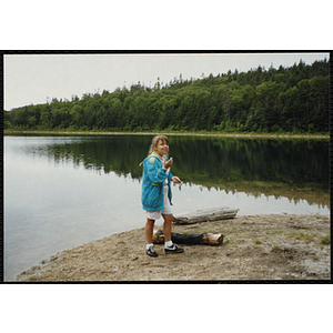 A girl stands on the shore of a pond