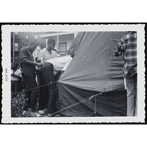A teenage boy peers inside a tent pitched in a yard as other boys look on