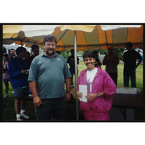 A woman and a man pose for a shot during the Battle of Bunker Hill Road Race as Executive Director Jerry Steimel (background, far left) stands in the background