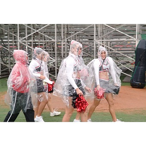 Cheerleaders in rain gear walk towards the field before the Homecoming game
