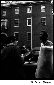 Umoja (Black student union) activist standing by car, wrapped in a sheepskin and talking to a white onlooker, at site of occupied administration building, Boston University