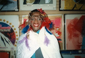 A Photograph of Marsha P. Johnson Wearing a Feather Headpiece and Draped in a Cloak
